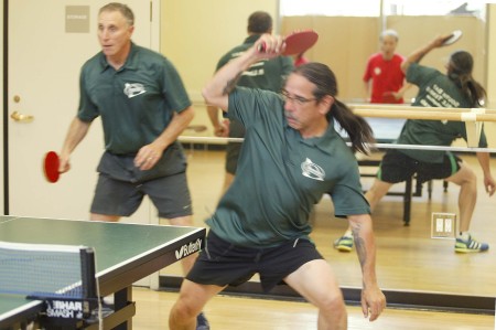 South Bay Eagle Paul Limburg waits in the back while his doubles partner Steve Sakurada loops aggressively against the Golden Ninjas seen reflected in the mirror.